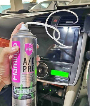 Hand holding a Flamingo A/C Pro car air conditioner cleaner can with extension tube attached, demonstrating targeted cleaning of automotive air conditioning vents and ducts.