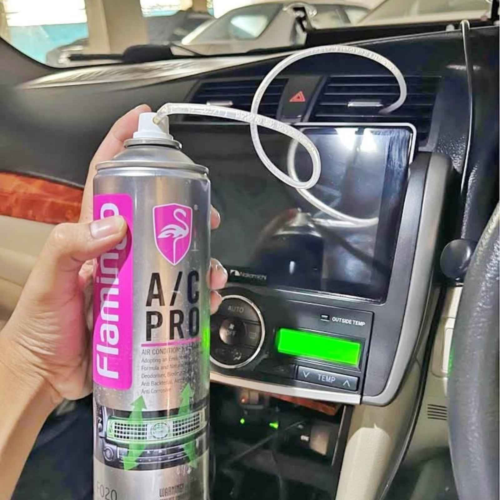 Hand holding a Flamingo A/C Pro car air conditioner cleaner can with extension tube attached, demonstrating targeted cleaning of automotive air conditioning vents and ducts.