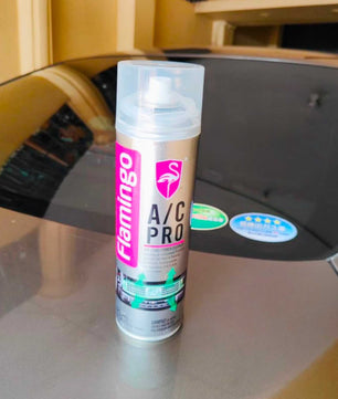 Flamingo A/C Pro car air conditioner cleaner aerosol can displayed on a vehicle surface, showcasing the product packaging for automotive AC cleaning and deodorizing.